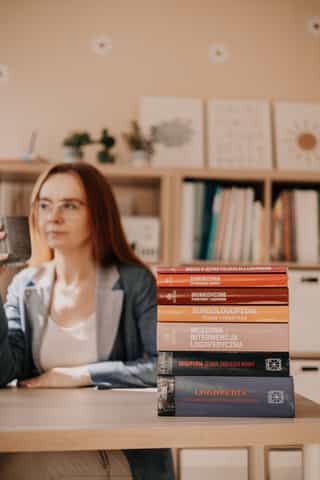 Zdjęcie przedstawiające widok gabinetu gdzie na pierwszym planie widać książki, a w tle kobietę wraz z regałami na książki